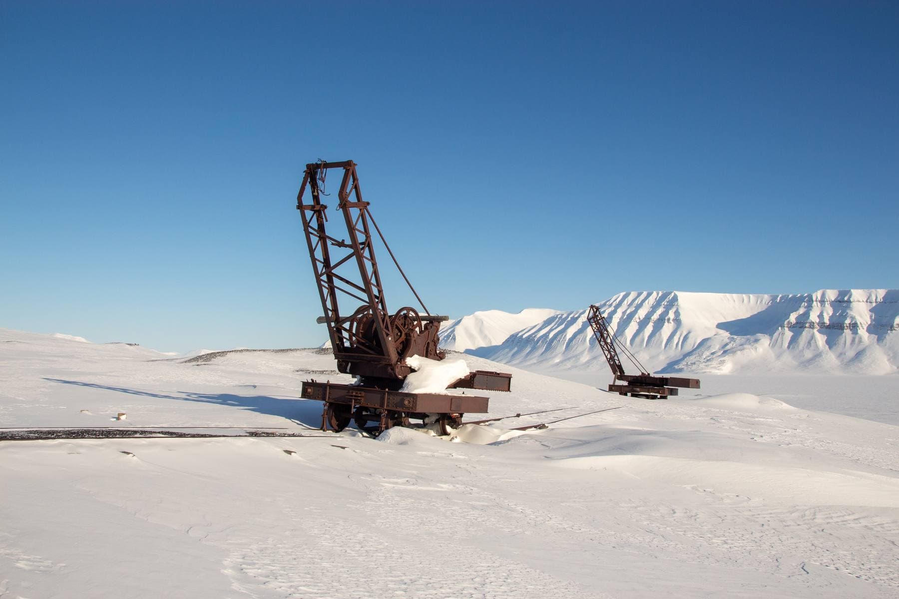 To rustne kraner står igjen i et vidt, snødekt landskap i Sveagruva på Svalbard